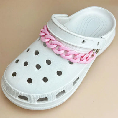 White clog shoe with a light pink chain accessory on a beige background