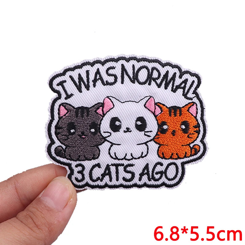 Embroidered patch with three cats and text 'I was normal 3 cats ago' held by a hand on a white background.