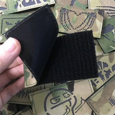 patch showing its Velcro backing   held over a collection of green tactical patches with designs