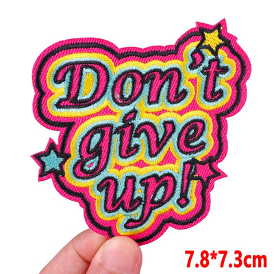 Embroidered patch with 'Don't give up!' text held by a hand on a white background
