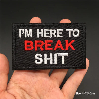 Text patch with 'I'm here to break shit' held in a hand against a dark background