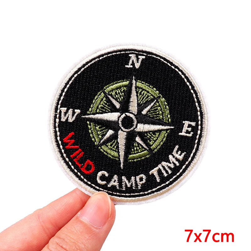 Patch with compass design and 'Wild Camp Time' text held by a hand, on a white background.