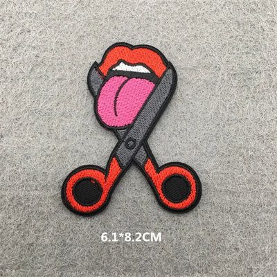Embroidered patch of scissors with a tongue design on a gray background