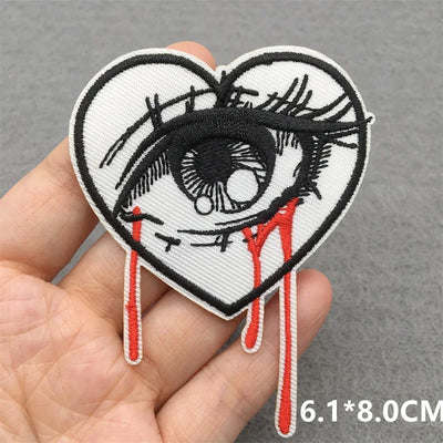 Heart-shaped patch with an eye design held by a hand on a gray background