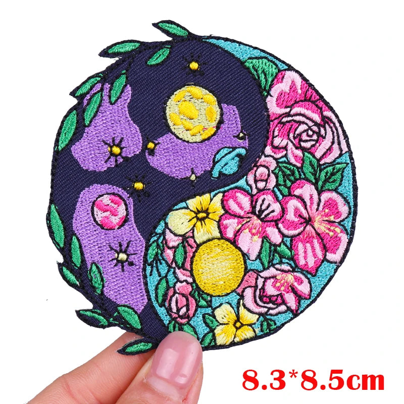 Circular embroidered patch with floral and moon designs held by a hand, on a white background.