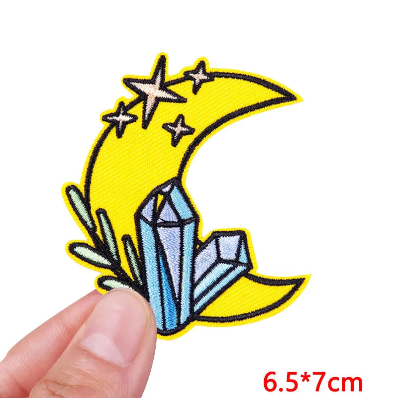 Embroidered patch with moon, stars, and crystals held by a hand on a white background.