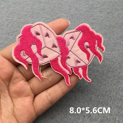 Two pink embroidered patches of a woman and a box held between fingers on a gray background.