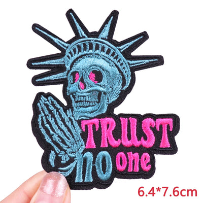 Embroidered patch with skeleton Statue of Liberty and 'Trust No One' text held by a hand.