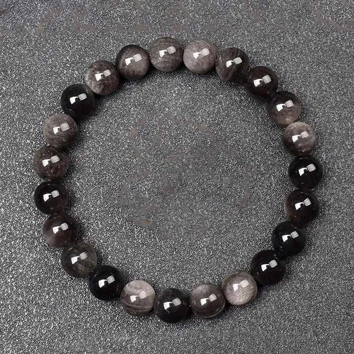 Round beaded bracelet with alternating dark and light beads on a gray surface