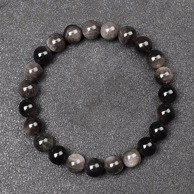 Round beaded bracelet with alternating dark and light beads on a gray surface