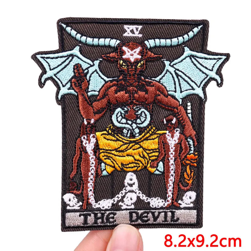 Embroidered patch of 'The Devil' from a tarot card held by a hand with measurement text.