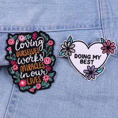 Two patches on a denim background, one with motivational text and flowers, the other with a heart and floral design.