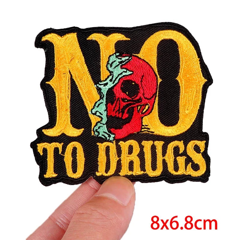 Embroidered patch with 'NO TO DRUGS' text and skull design held by a finger on a white background.