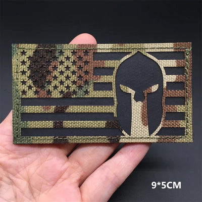 USA Camouflage flag patch with Spartan helmet design held in a hand against a dark background
