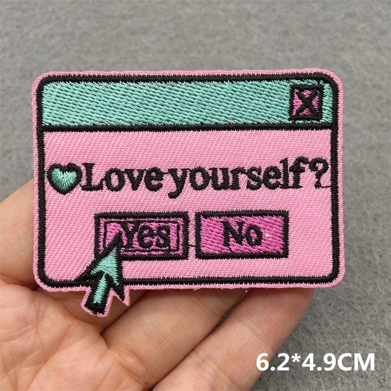 Pink patch with 'Love yourself?' question and 'Yes'/'No' options held in a hand against a gray background.