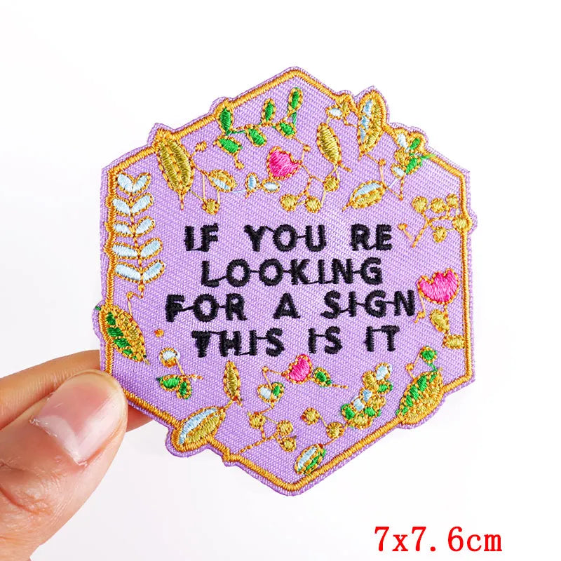 Embroidered patch with decorative border and text held by a hand on a white background