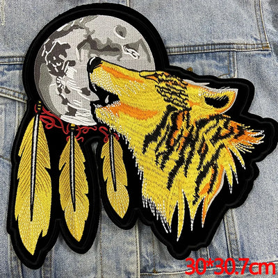 Embroidered patch of a wolf howling with feathers on a denim background
