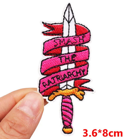 Patch with 'Smash the Patriarchy' text held by a hand on a white background