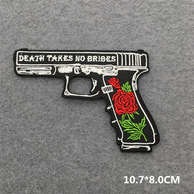Embroidered patch of a gun with roses and 'Death Takes No Bribes' text on a gray background