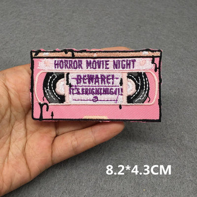 Pink cassette tape patch with text held by a hand on a gray background