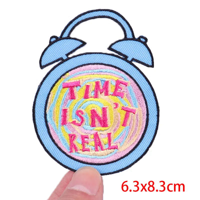 Patch with 'Time Isn't Real' text on a blue alarm clock design, held by a hand.