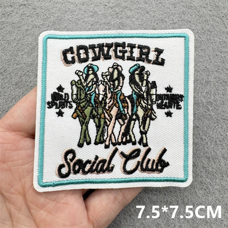 Embroidered patch with 'Cowgirl Social Club' design held in a hand on a gray background.