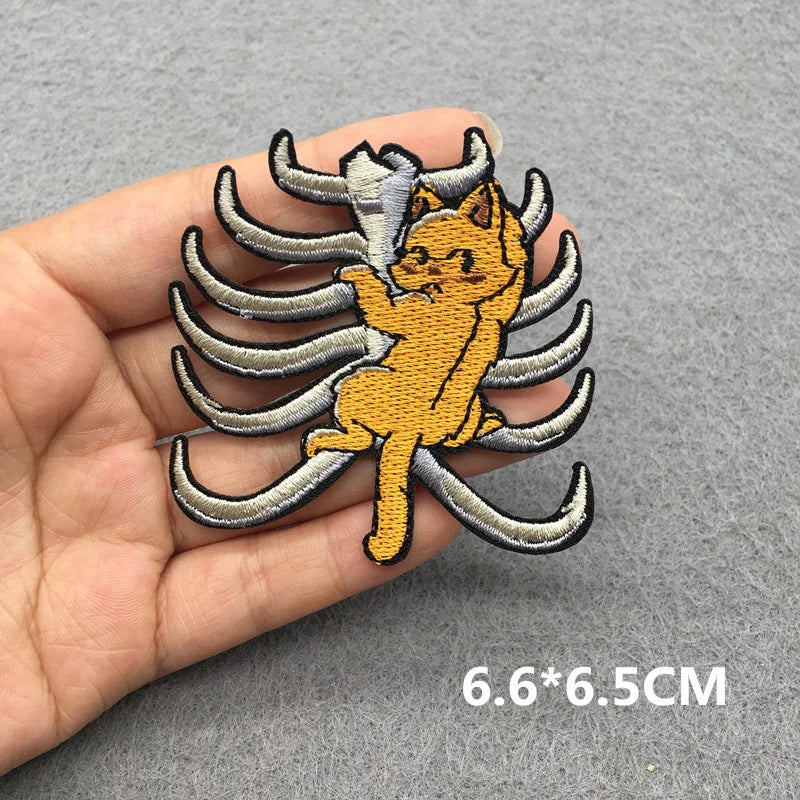 Embroidered patch of a cat with wings held in a hand on a gray background