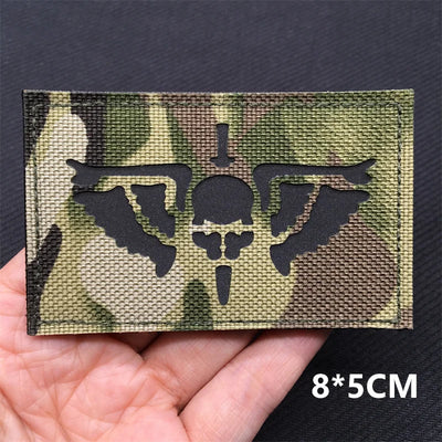 Camouflage patch with skull and crossbones design held in a hand against a dark background