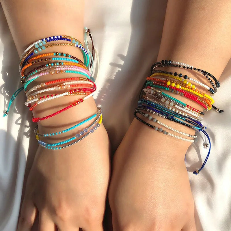 Two wrists with colorful beaded bracelets on a light background