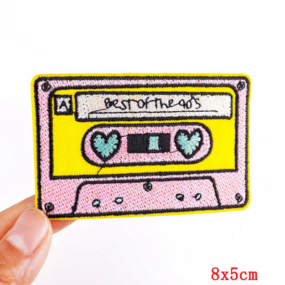 Embroidered patch of a cassette tape with 'Best of the 90s' text held by a hand on a white background.