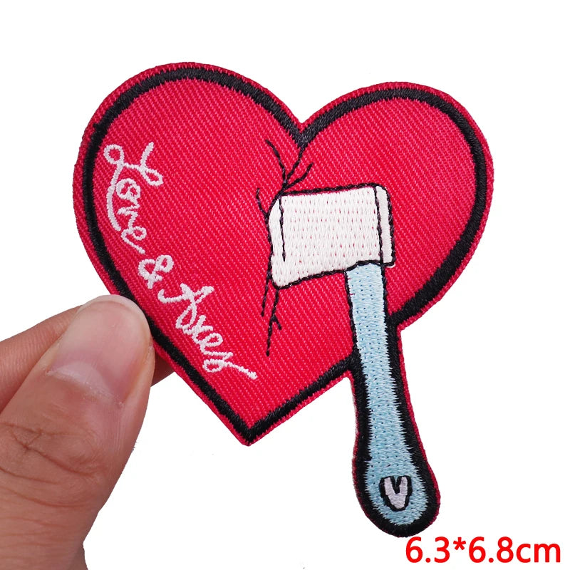 Heart-shaped patch with an axe and 'Love & Axes' text, held by a hand.