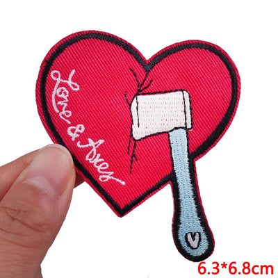 Heart-shaped patch with an axe and 'Love & Axes' text, held by a hand.