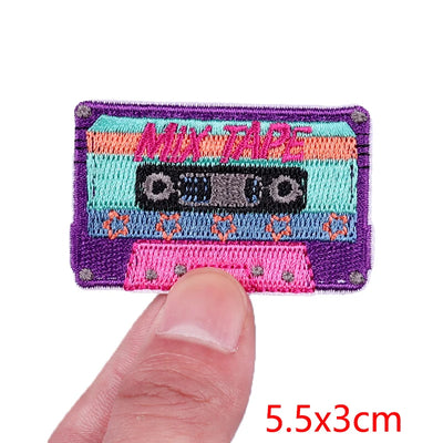 Colorful woven patch of a cassette tape with 'Mix Tape' text, held between fingers.
