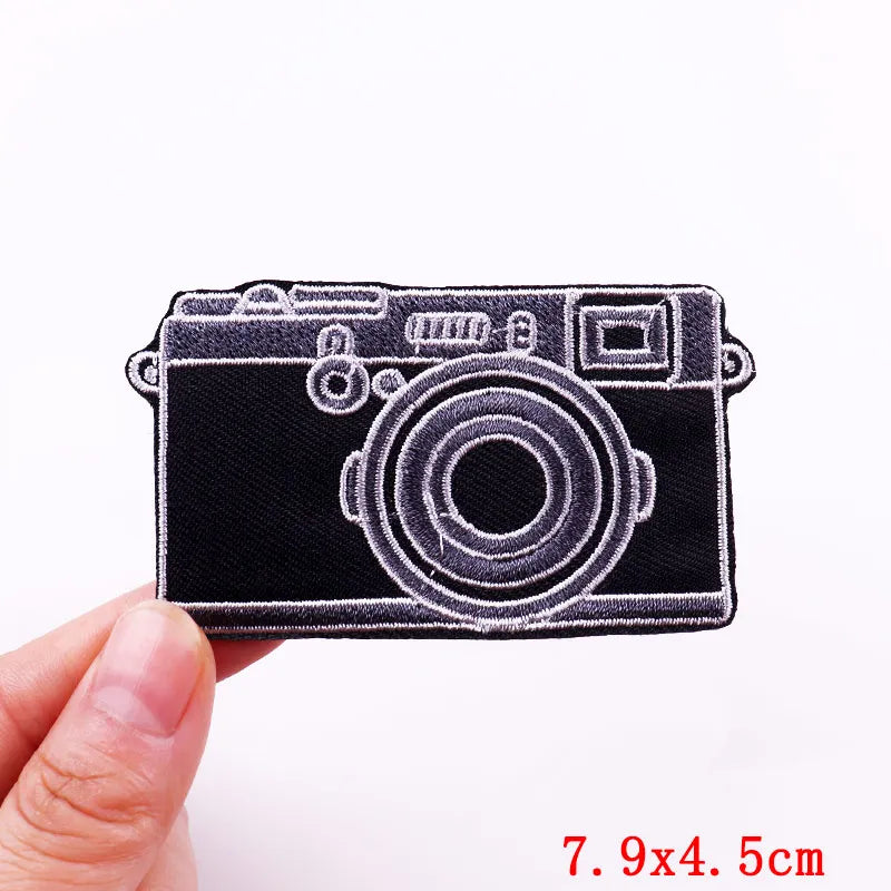 Camera-shaped patch held by a hand with size measurement on a white background