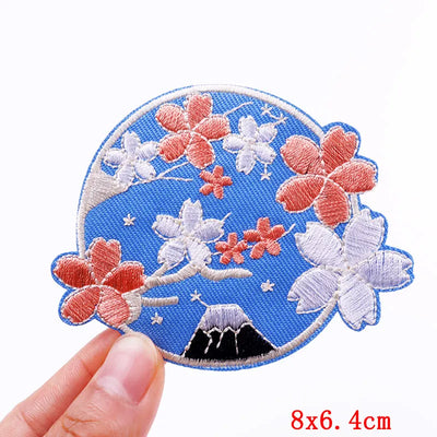 Embroidered patch with flowers and Mount Fuji on a blue background held by a hand.