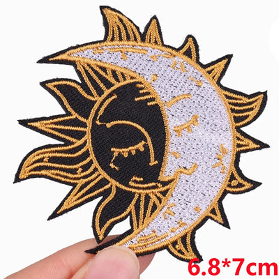 Embroidered patch of a sun and moon design held by a hand on a white background.