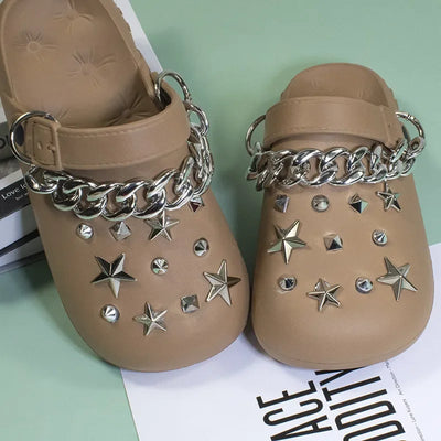 Beige clogs with silver chain and star embellishments on a light green surface.