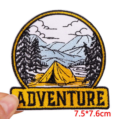 Embroidered patch with a tent and mountains design, labeled 'Adventure', held by a hand.