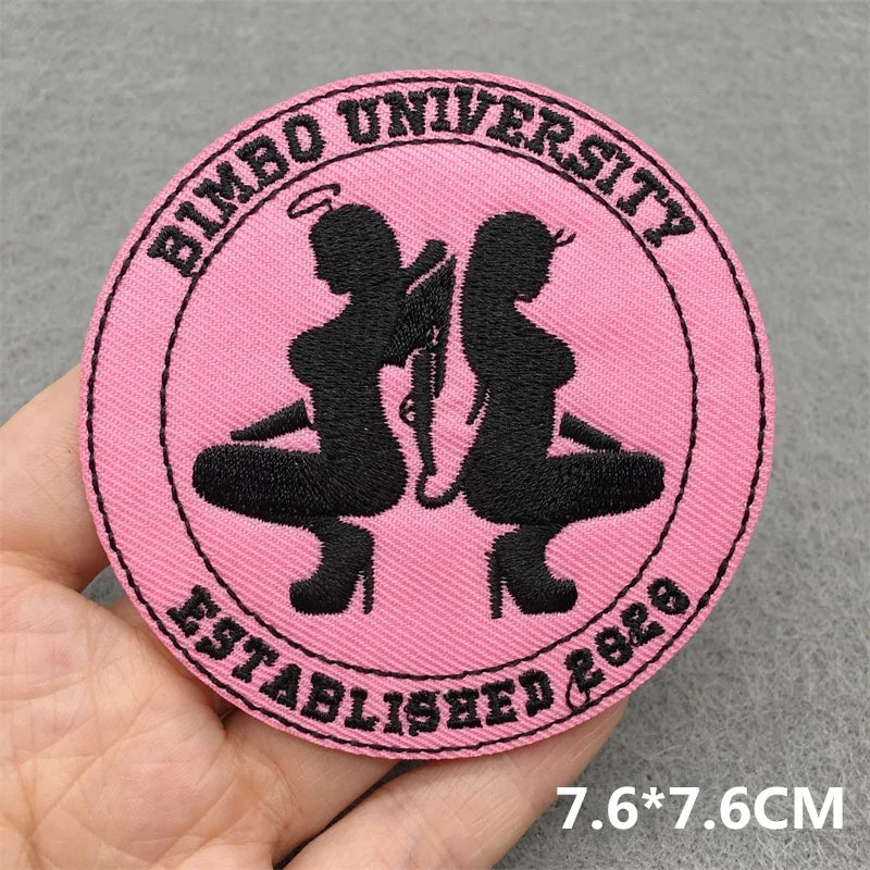 Pink patch with black silhouettes and text held by a hand on a gray background