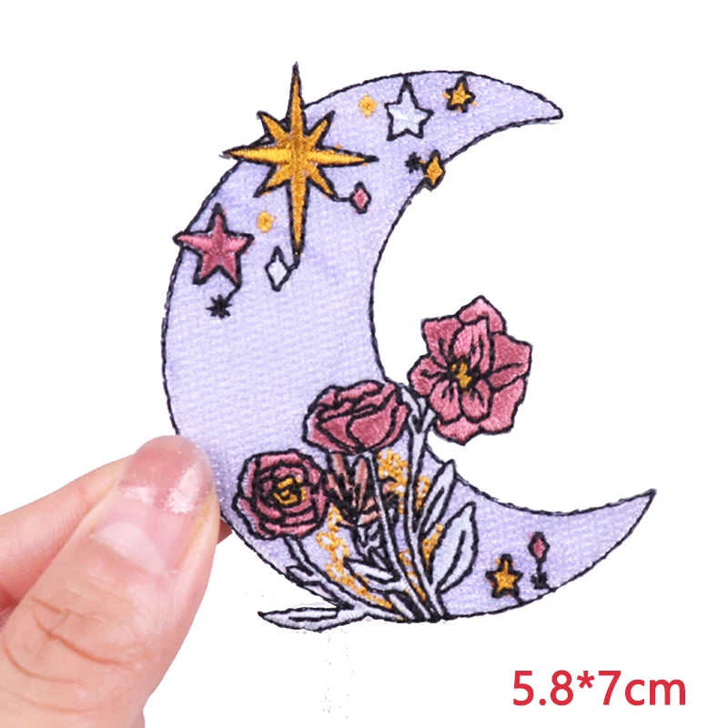 Decorative patch with moon, stars, and flowers held by a hand on a white background