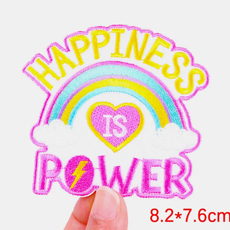 Embroidered patch with rainbow, heart, and text 'Happiness is Power' held by a hand.