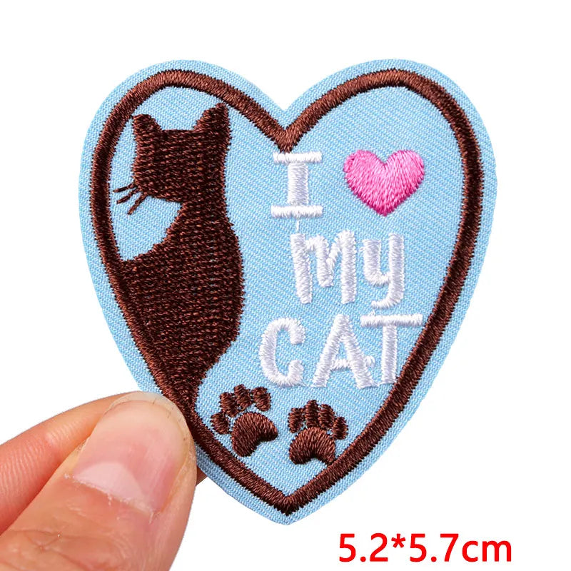 Heart-shaped patch with a cat silhouette and 'I love my cat' text held by a hand.