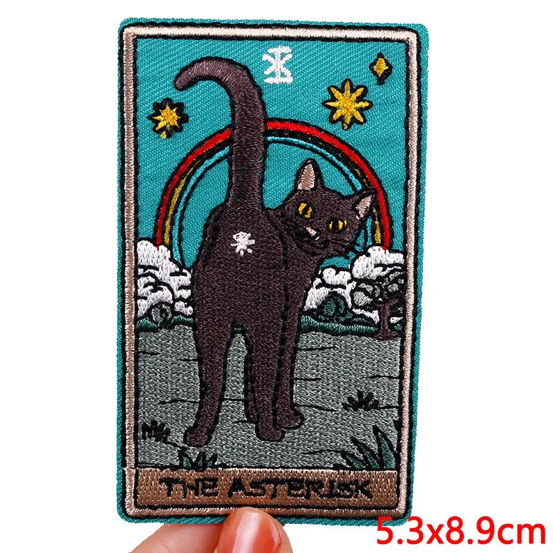 Embroidered patch of a black cat with a rainbow and stars on a blue background, held by a hand.