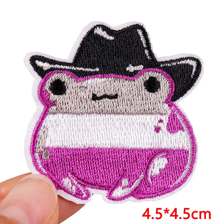 Embroidered patch of a cartoon character with a black hat held by a hand on a white background.