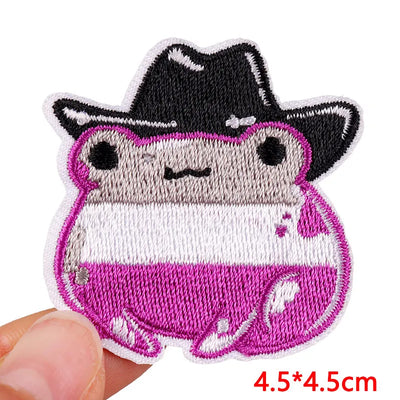 Embroidered patch of a cartoon character with a black hat held by a hand on a white background.