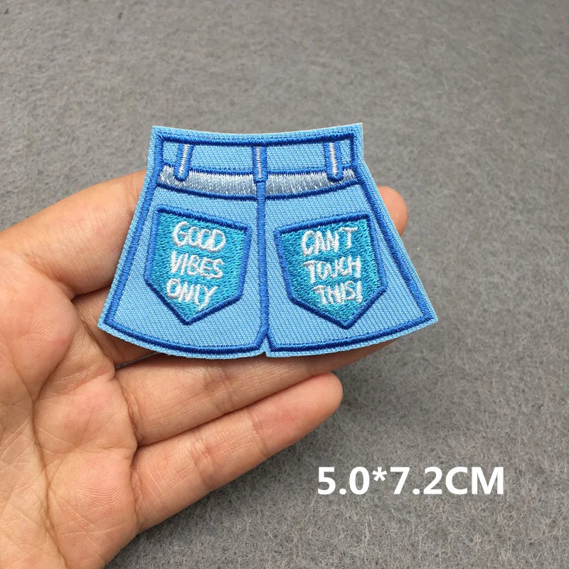 Blue denim-style patch with text held in a hand on a gray background