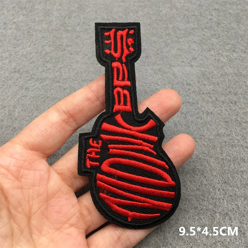 Red and black guitar-shaped patch held in a hand against a gray background