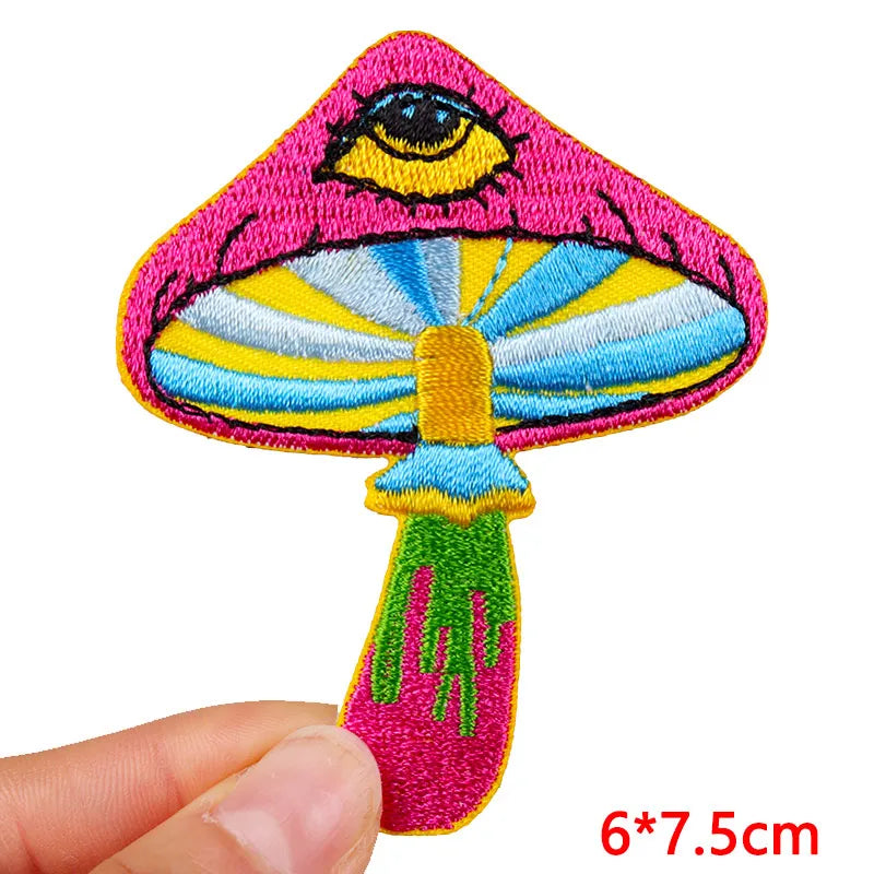 Colorful embroidered mushroom patch held by a hand on a white background