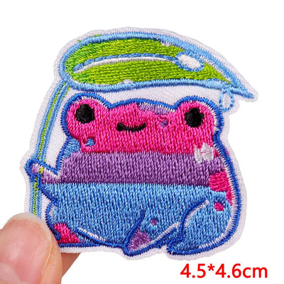 Embroidered patch of a pink and blue creature with a green hat held by a hand, size 4.5*4.6cm.