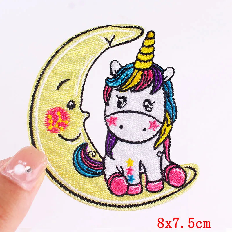 Embroidered patch of a unicorn and moon with colorful hair held by a hand.